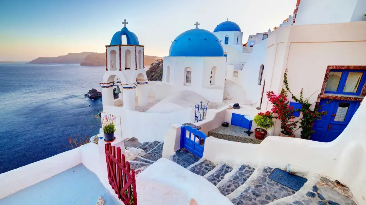 Białe domy z niebieskimi kopułami kościołów na tle morza i wysp. Widok na kaldera Santorini o zachodzie słońca.