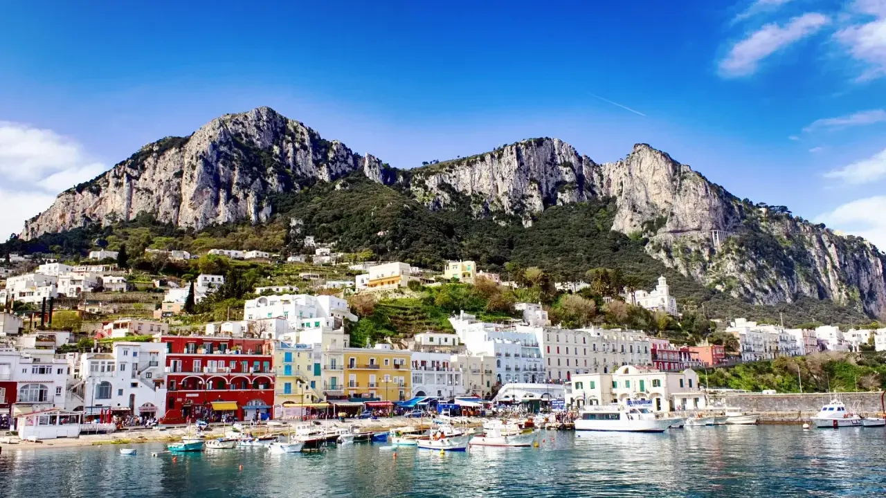 Kolorowe budynki portu na Capri, z górami w tle. Idealne miejsce na wakacje, gdzie można podziwiać widoki i cieszyć się słońcem.