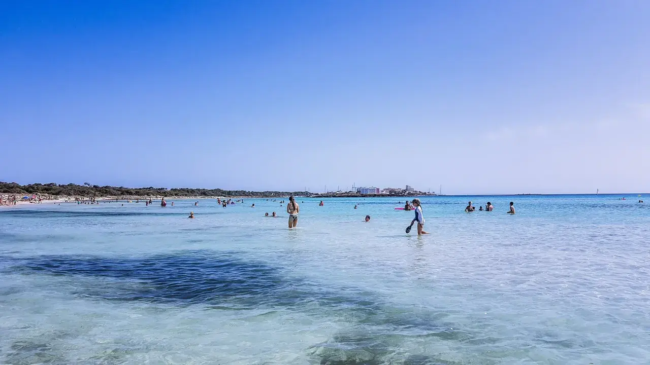 Słoneczny dzień na plaży Es Trenc. Ludzie kąpią się w krystalicznie czystej wodzie, ciesząc się wakacjami.