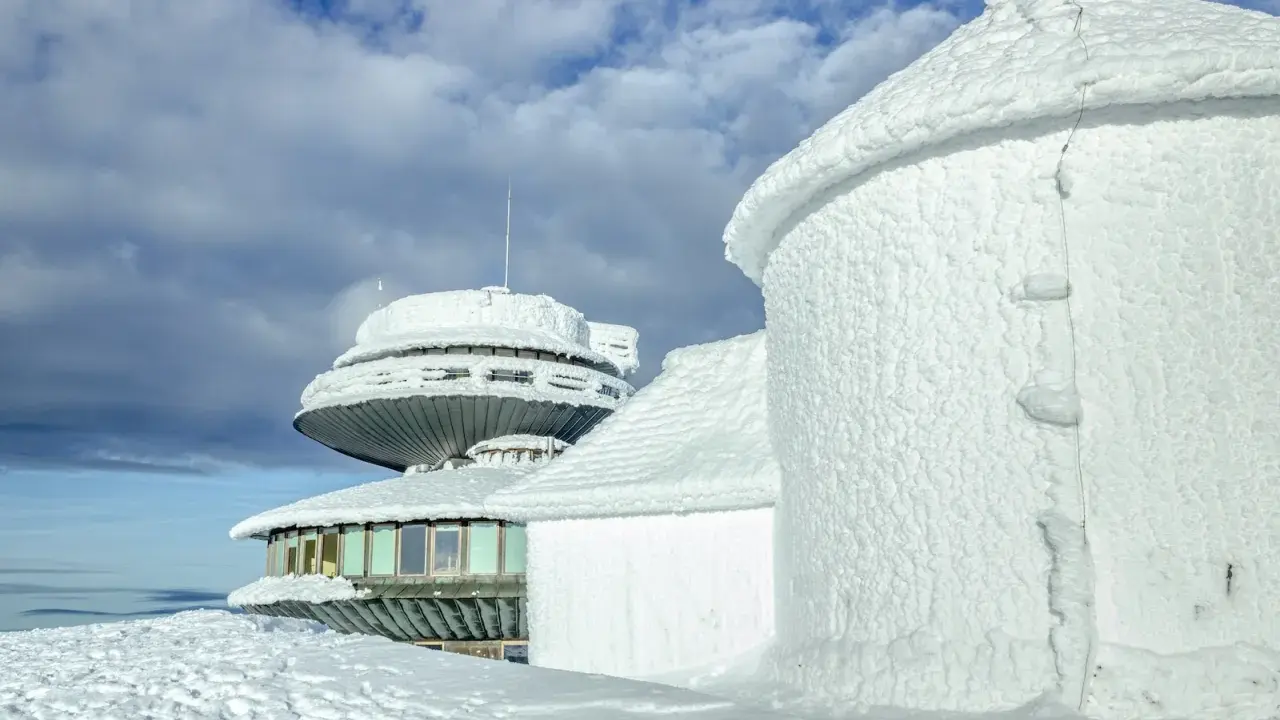Zimowe krajobrazy na Śnieżce. Budynki obserwatorium pokryte lodem i śniegiem, niebo z chmurami.