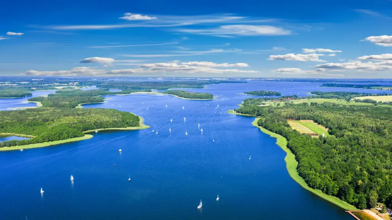 Malownicze mazury jeziora z licznymi wyspami i żaglówkami pod błękitnym niebem.