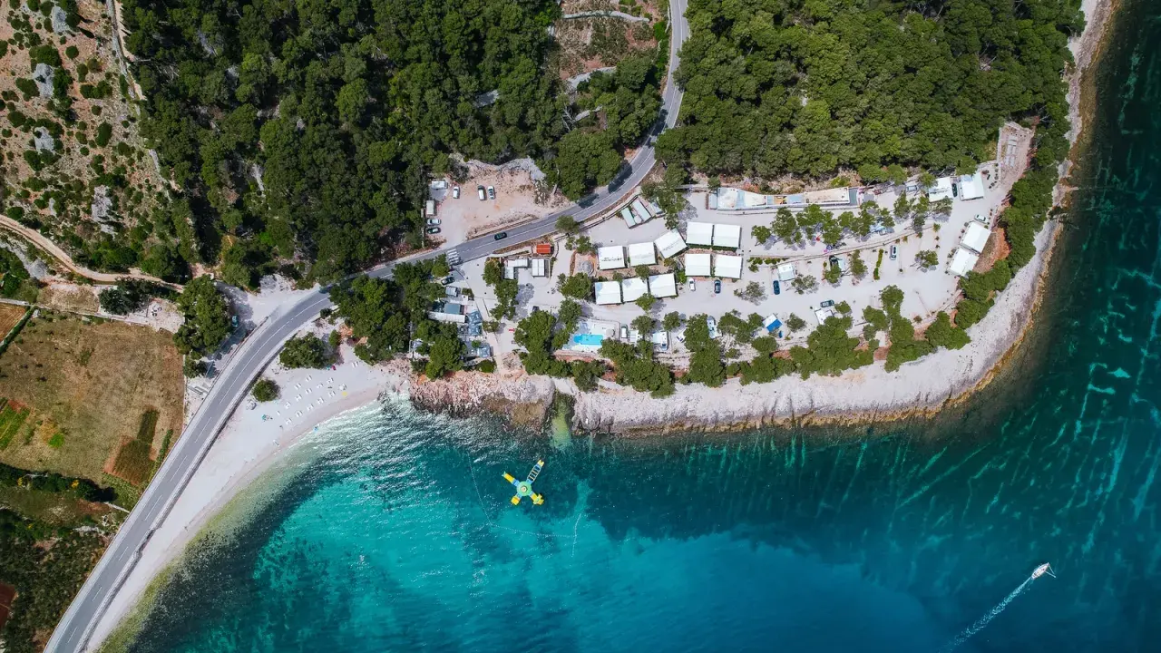 Widok z lotu ptaka na Hvar camping: białe domki, basen, plaża i turkusowe morze. Idealne miejsce na wakacje.