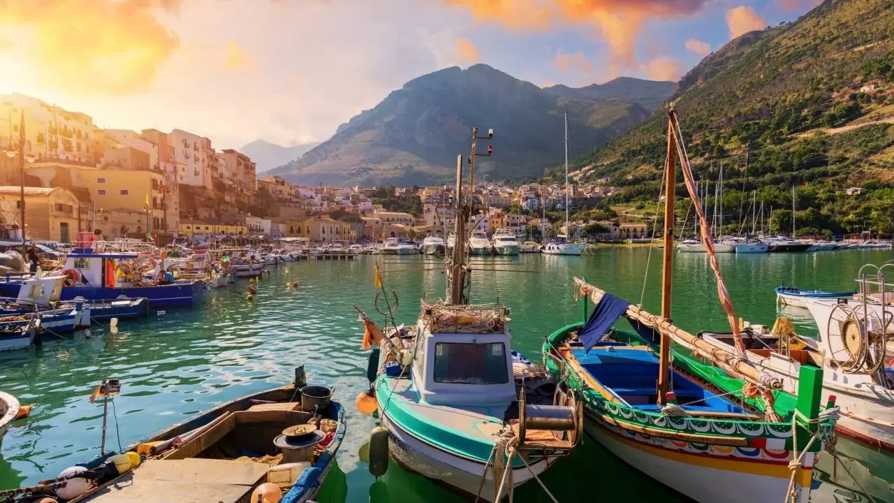 Malowniczy port w Trapani, idealne miejsce na zwiedzanie. Łodzie kołyszą się na wodzie, a w tle widać góry i kolorowe budynki.