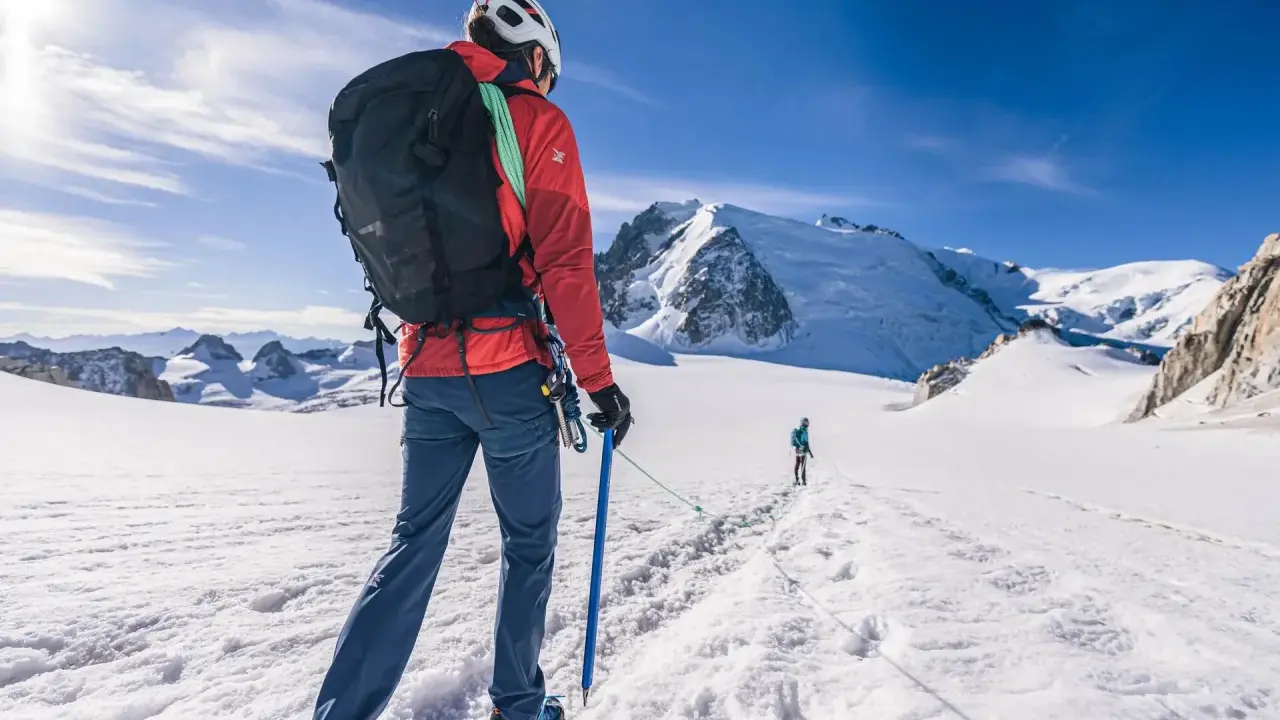 Alpinista z czekanem w ręku, ucząc się, jak trzymać czekan, na tle ośnieżonych gór.