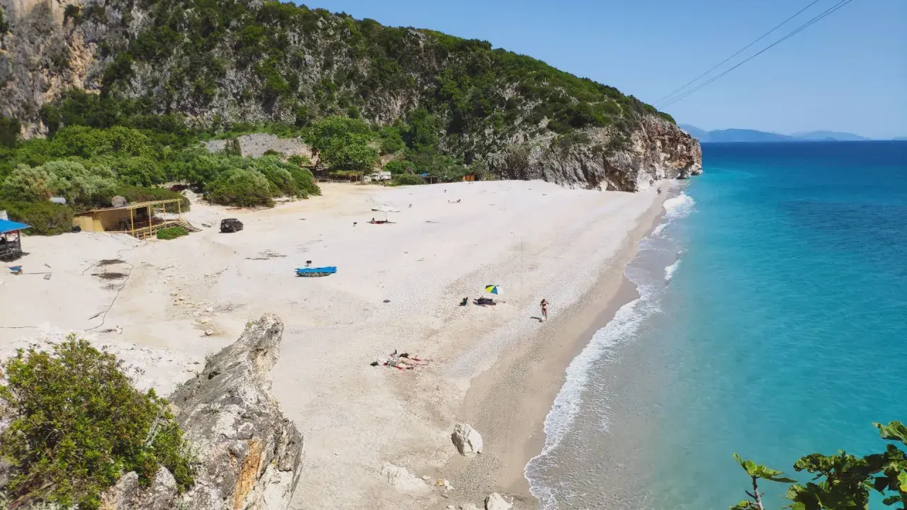 Malownicza plaża Gjipe z turkusową wodą, skalistymi klifami i kilkoma turystami relaksującymi się na piasku.