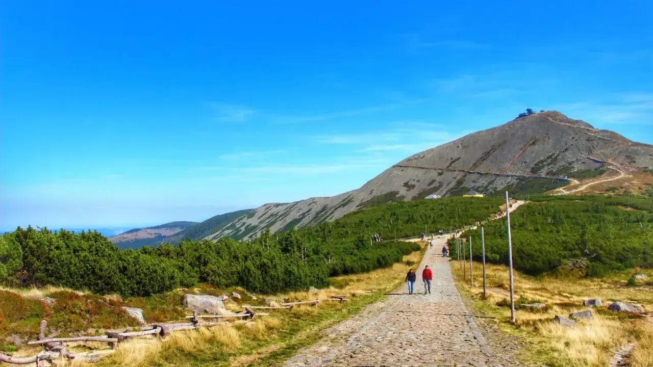 Kamienista ścieżka prowadzi na szczyt Śnieżki. Turyści idą w kierunku górskiej panoramy.