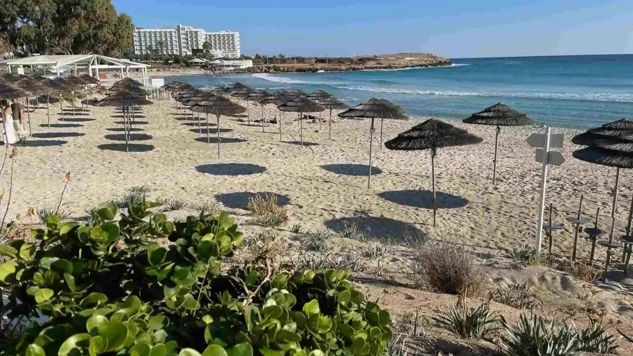 Plaża na Cyprze z rzędami parasoli i hotel w tle. Idealne miejsce na relaks na jednych z cypr best beaches.