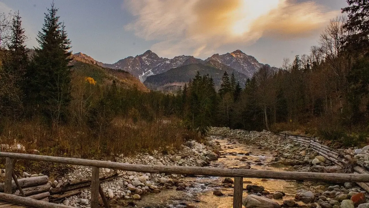 Jesienne Tatry w październiku. Drewniany mostek nad kamienistym potokiem, w tle góry i lasy.