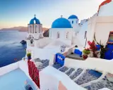 Białe domy z niebieskimi kopułami kościołów na tle morza i wysp. Widok na kaldera Santorini o zachodzie słońca.
