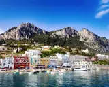 Kolorowe budynki portu na Capri, z górami w tle. Idealne miejsce na wakacje, gdzie można podziwiać widoki i cieszyć się słońcem.