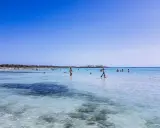Słoneczny dzień na plaży Es Trenc. Ludzie kąpią się w krystalicznie czystej wodzie, ciesząc się wakacjami.