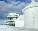 Zimowe krajobrazy na Śnieżce. Budynki obserwatorium pokryte lodem i śniegiem, niebo z chmurami.