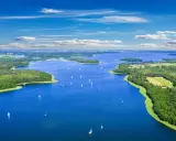 Malownicze mazury jeziora z licznymi wyspami i żaglówkami pod błękitnym niebem.