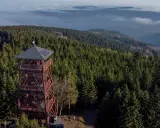 Wieża widokowa na Orlicy szczyt, otoczona gęstym lasem świerkowym, góruje nad morzem mgieł i pagórków.