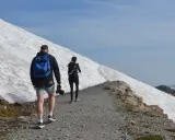 Spacerzy po szlaku w kierunku najwyższego szczytu Australii. Na zboczu widać śnieg i skały.