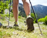 Nogi w butach trekkingowych i kijki wspierają chodzenie po górskim szlaku.