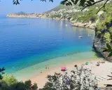 Malownicza zatoka z turkusową wodą i kamienistą plażą. W oddali widać mury Starego Miasta Dubrownik. Idealne plaże Dubrownik na relaks.