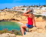 Kobieta w kapeluszu podziwia malownicze portugalia wybrzeże algarve z białymi domkami i turkusową wodą.