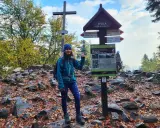 Uśmiechnięta turystka na szczycie Łysica (614 m n.p.m.) wśród kamieni i jesiennych liści. Widoczny drewniany krzyż i drogowskazy.