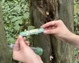 Ręce trzymają pojemnik i zeszyt z napisem "GEOCACHING LOGBOOK". To wyjaśnia, geocaching co to jest: poszukiwanie ukrytych skarbów.