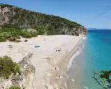 Malownicza plaża Gjipe z turkusową wodą, skalistymi klifami i kilkoma turystami relaksującymi się na piasku.