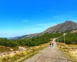 Kamienista ścieżka prowadzi na szczyt Śnieżki. Turyści idą w kierunku górskiej panoramy.