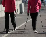 Dwie osoby w czerwonych kurtkach i czarnych spodniach maszerują z kijki do nordic walking.