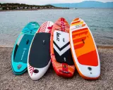 Cztery kolorowe deski SUP dla dzieci stoją na plaży, gotowe na wodne przygody.
