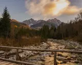 Jesienne Tatry w październiku. Drewniany mostek nad kamienistym potokiem, w tle góry i lasy.