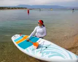 Kobieta z wiosłem przygotowuje się do wyprawy na desce sup touring. W tle widać spokojne morze i góry.