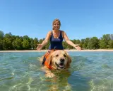 Kobieta z radością wita pływającego w jeziorze golden retrievera w kamizelce ratunkowej. Czy każdy pies umie pływać? Ten na pewno tak!
