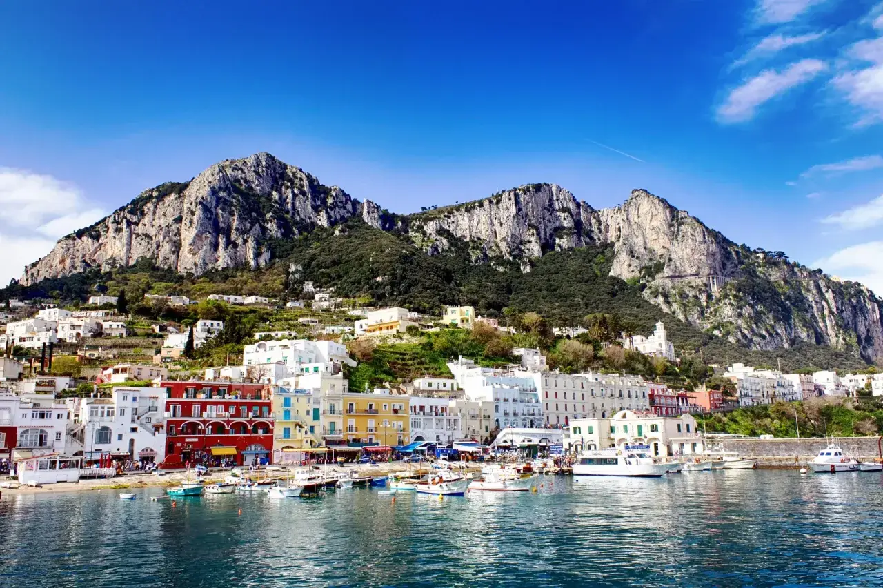 Kolorowe budynki portu na Capri, z górami w tle. Idealne miejsce na wakacje, gdzie można podziwiać widoki i cieszyć się słońcem.