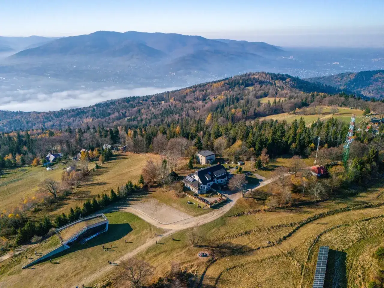 Widok z lotu ptaka na górski krajobraz jesienią. Widać domy, lasy i dolinę z mgłą. To czupel najładniejszy szlak.