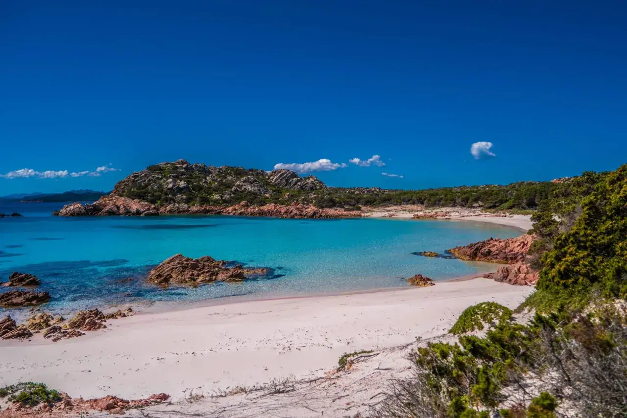Spiaggia rosa z turkusową wodą i skalistymi formacjami.