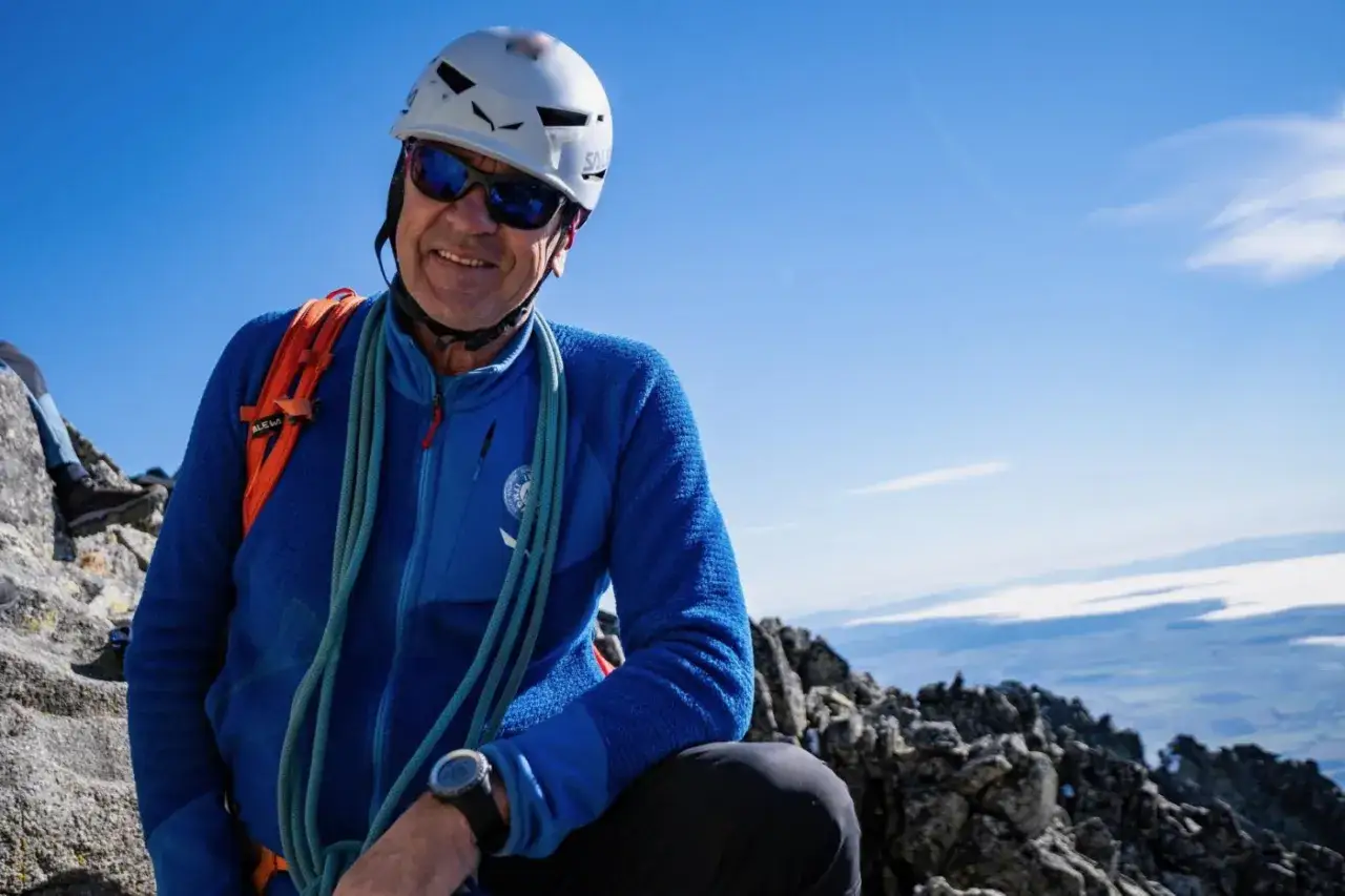 Szczęśliwy alpinista w kasku i okularach przeciwsłonecznych na tle błękitnego nieba, z liną wspinaczkową na ramieniu. Widok z Gerlach szczytu zapiera dech w piersiach.
