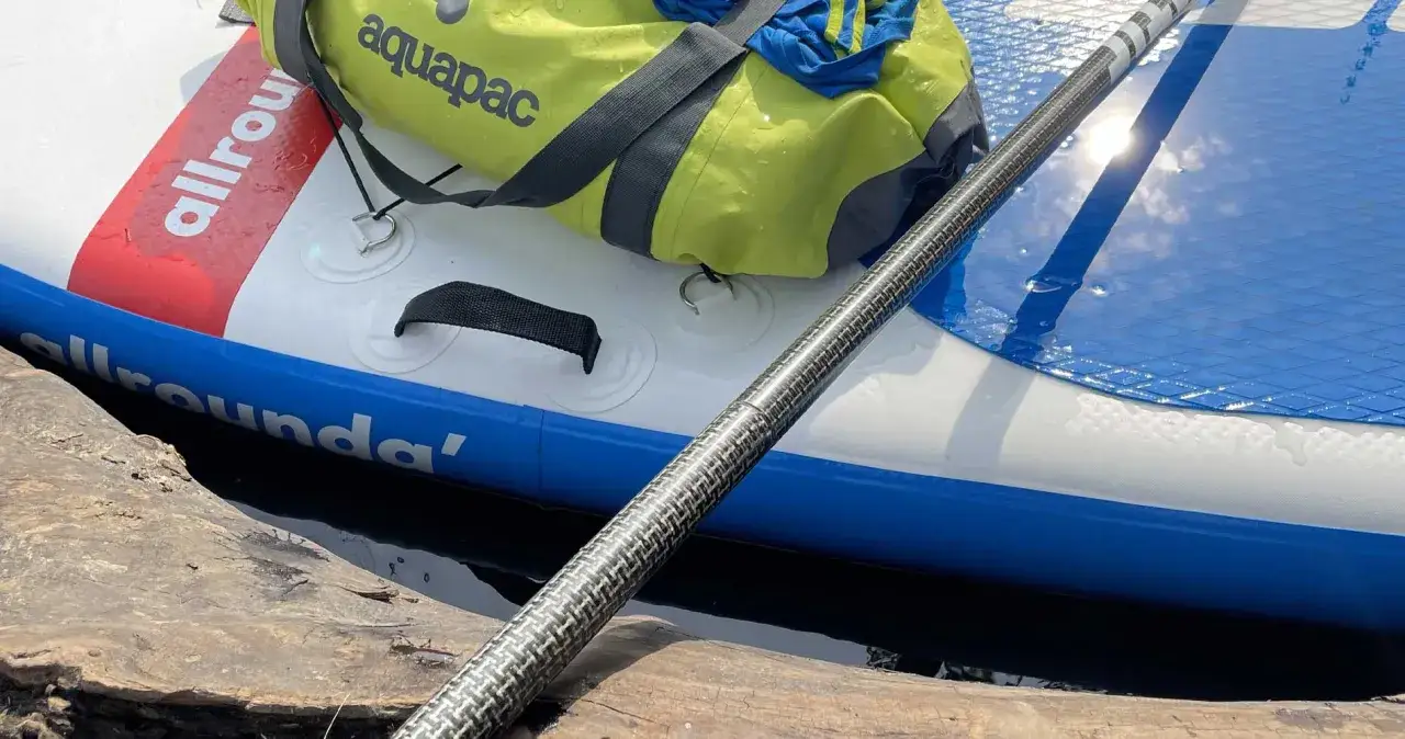 Deska SUP i wiosło czekają na przygodę na górskiej rzece. Zielona torba aquapac gotowa na wodne wyzwania.