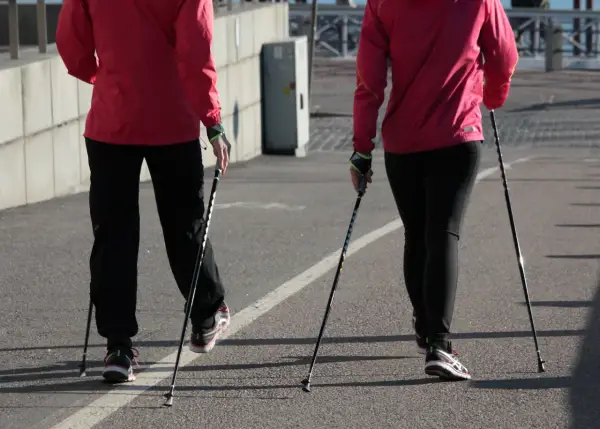 Dwie osoby w czerwonych kurtkach i czarnych spodniach maszerują z kijki do nordic walking.
