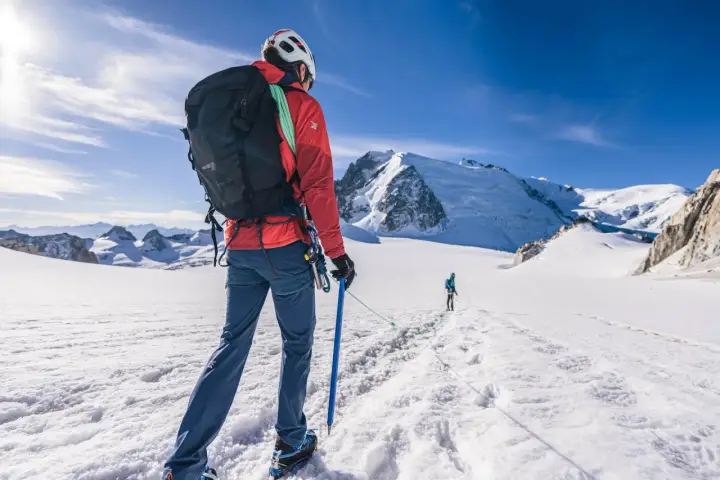 Alpinista z czekanem w ręku, ucząc się, jak trzymać czekan, na tle ośnieżonych gór.