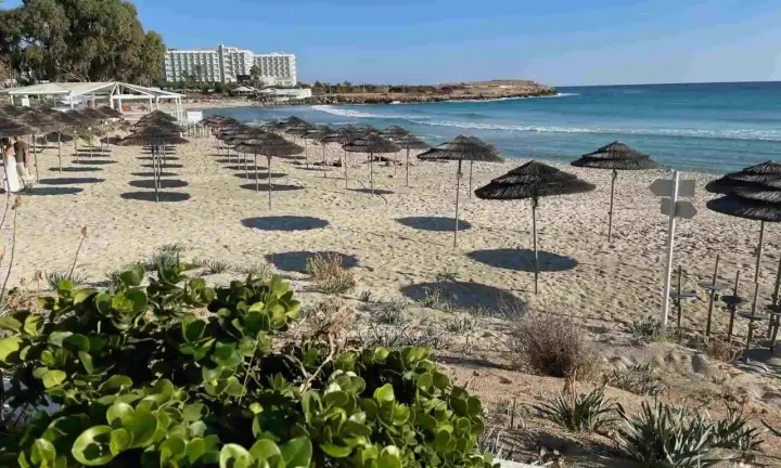 Plaża na Cyprze z rzędami parasoli i hotel w tle. Idealne miejsce na relaks na jednych z cypr best beaches.